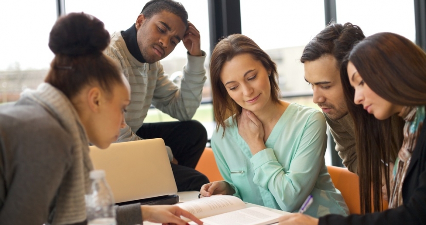Teens at a table looking at a book Teens at a table looking at a book