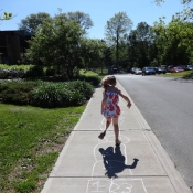 Young girl plays hopscotch on a chalk drawn board on the sidewalk
