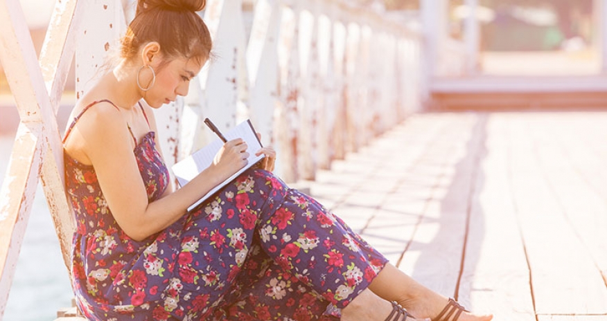 Write On girl sitting on a bridge writing on her notebook